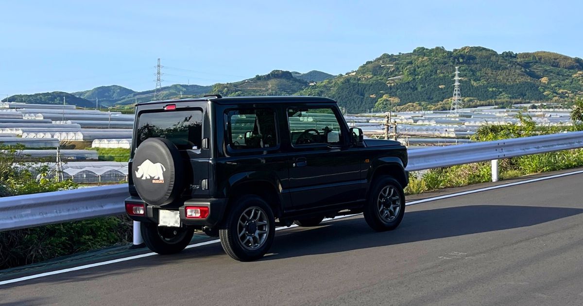 朝日に照らされたスズキ ジムニーJB64 XC（黒）が九州の山あいを背景に輝く様子