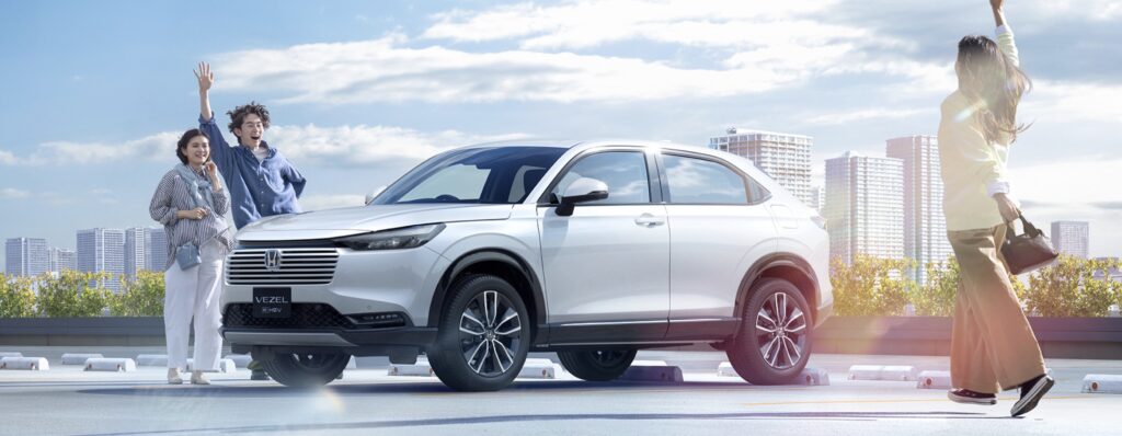 後部座席が広いおすすめコンパクトSUV、ホンダ・ヴェゼルの横からの写真。家族が楽しそうに手を振っている。