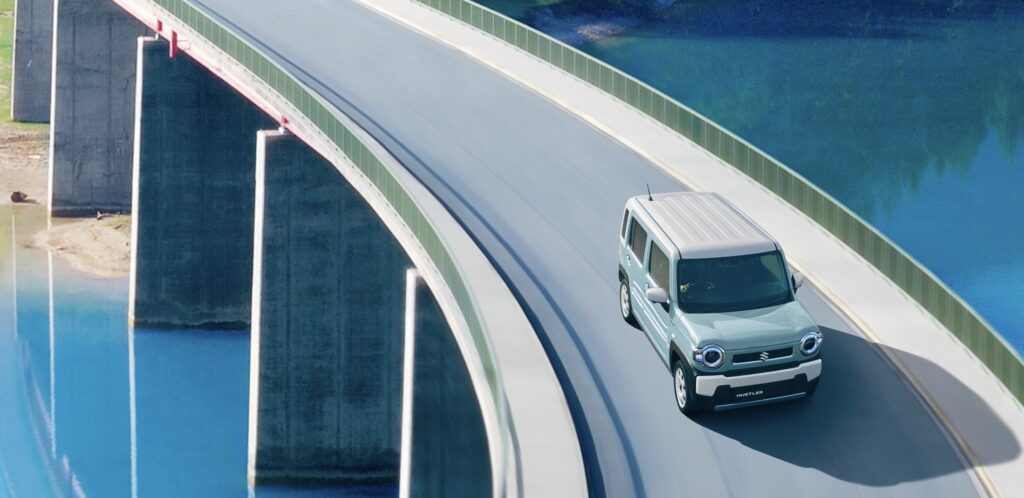 カーブした橋を走行する水色のスズキ ハスラー。この記事では、このような峠道や高速道路で「ハスラーは運転しにくい」と感じる具体的な理由を、ジムニー乗りの視点から解説します。