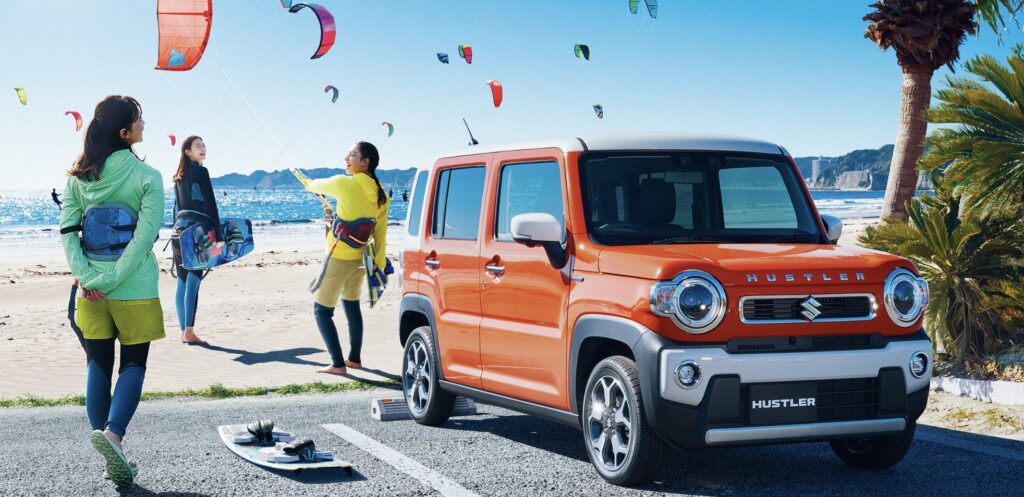 後部座席が広く常識を覆すおすすめ軽SUV、オレンジ色のスズキ ハスラーと海辺で楽しむ人々。