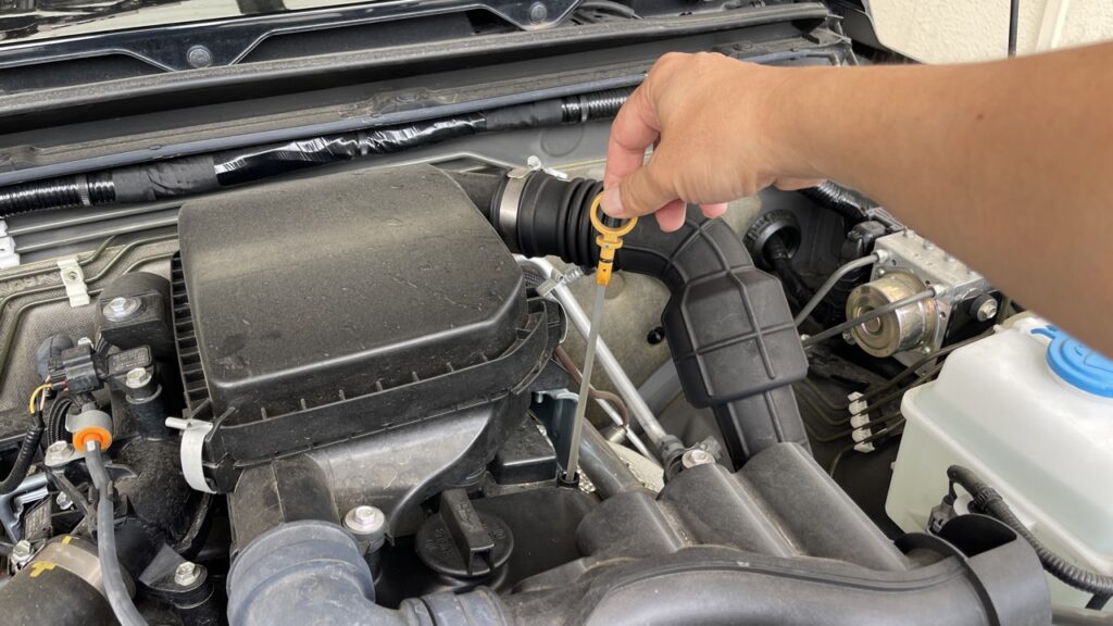 筆者が愛車ジムニーJB64のエンジンルームを開け、純正オイルで管理されたオイルレベルゲージを実際に引き抜いて点検している手元。