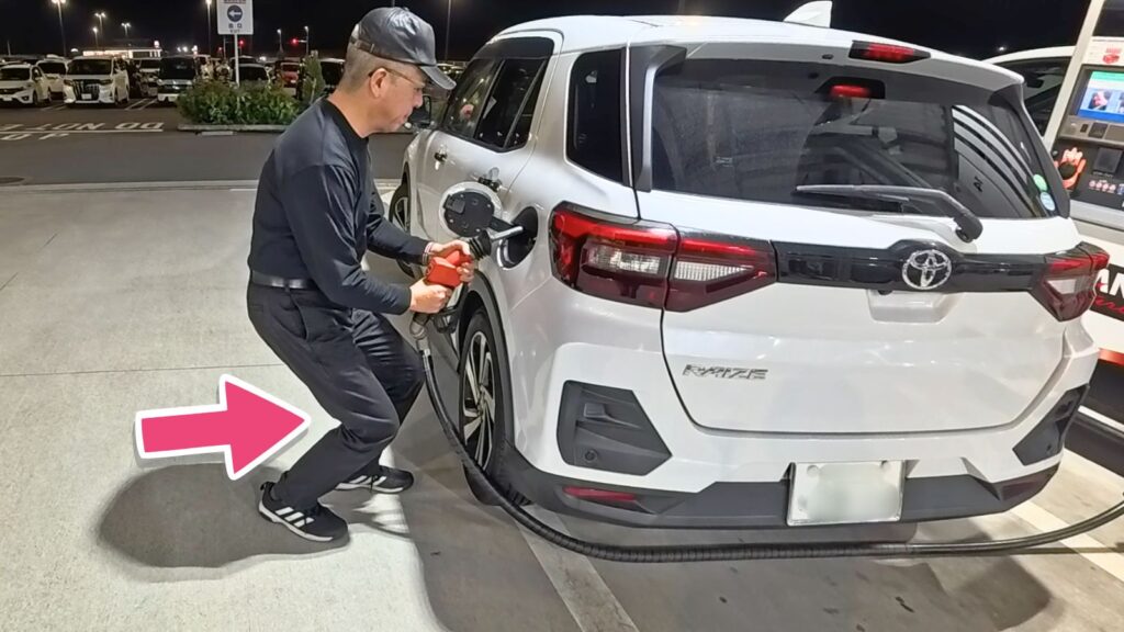 セルフガソリンスタンドにて、トヨタ・ライズ（SUV）に給油する際、ひざを曲げて重心を安定させ、両手でノズルを保持する40年以上無事故のプロ（緒方智幸＝むらなす）の全身写真。足腰を使ったスマートな給油フォームを実演。