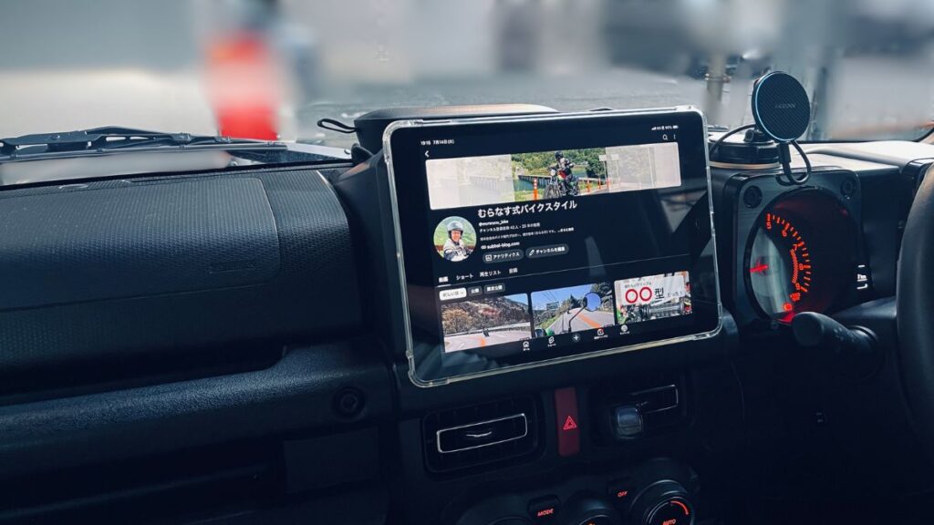 ジムニーJB64型の助手席側から撮影した、2DINスペースにマグネット固定されたiPadと右隣のメーターパネル。フロントガラス越しの背景は白くぼかされています。